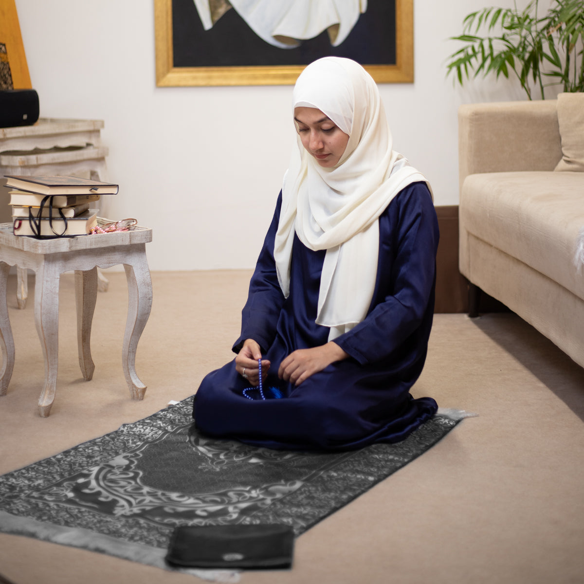 a woman is carrying prayer beads while sitting on a prayer mat in black color
