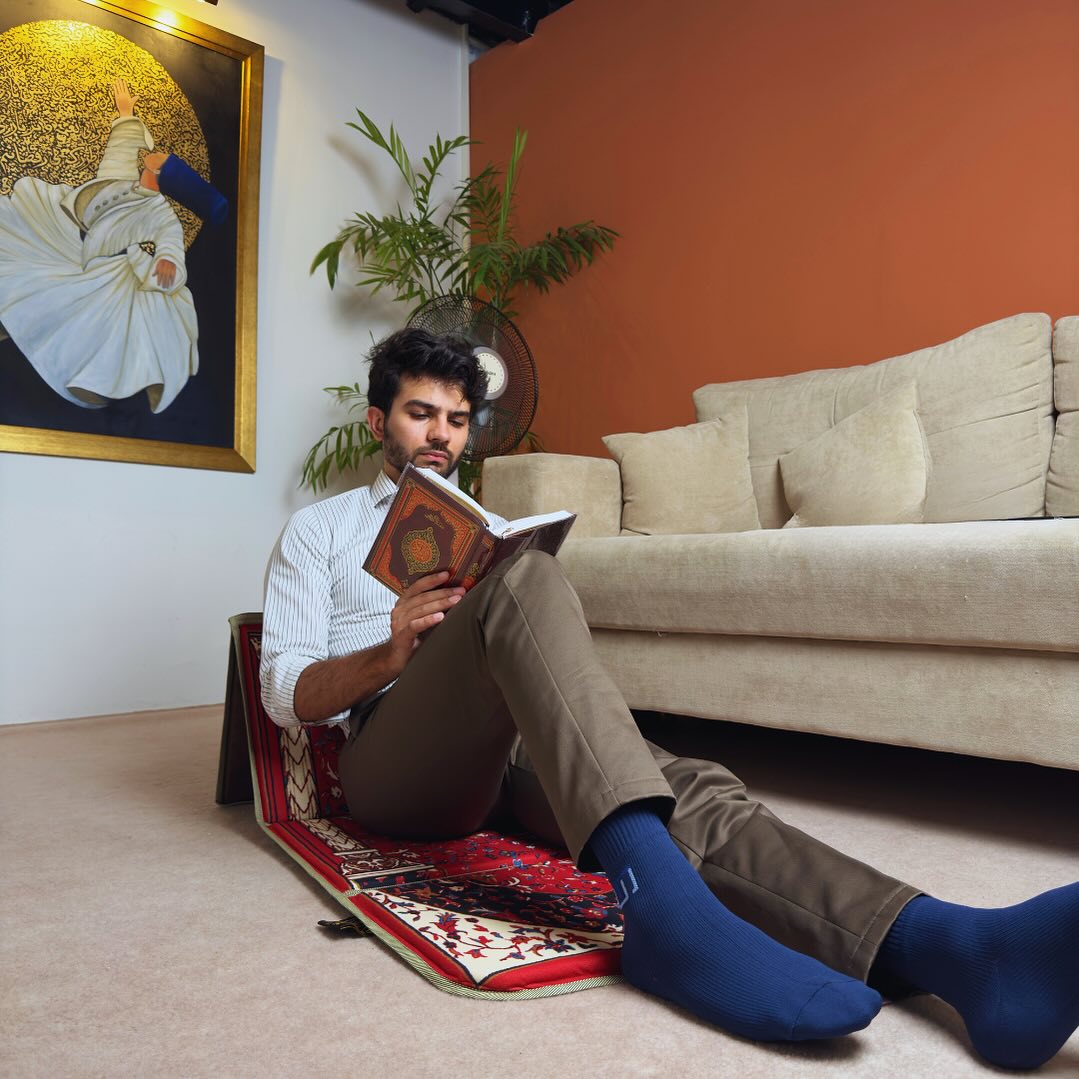 A man sitting with the help of a backrest on lava red ebadat prayer rug