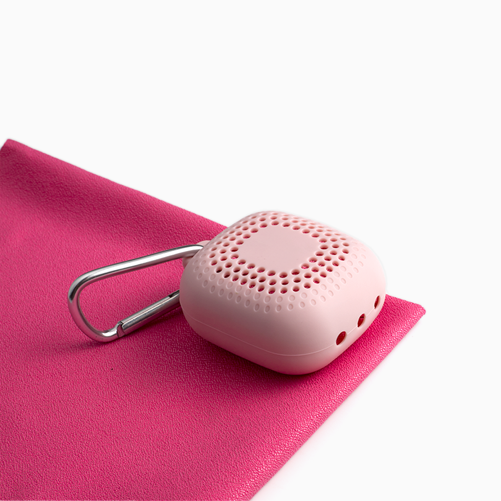 A portable wudhu towel in pink color, laid out flat with a compact green case with a carabiner clip on top