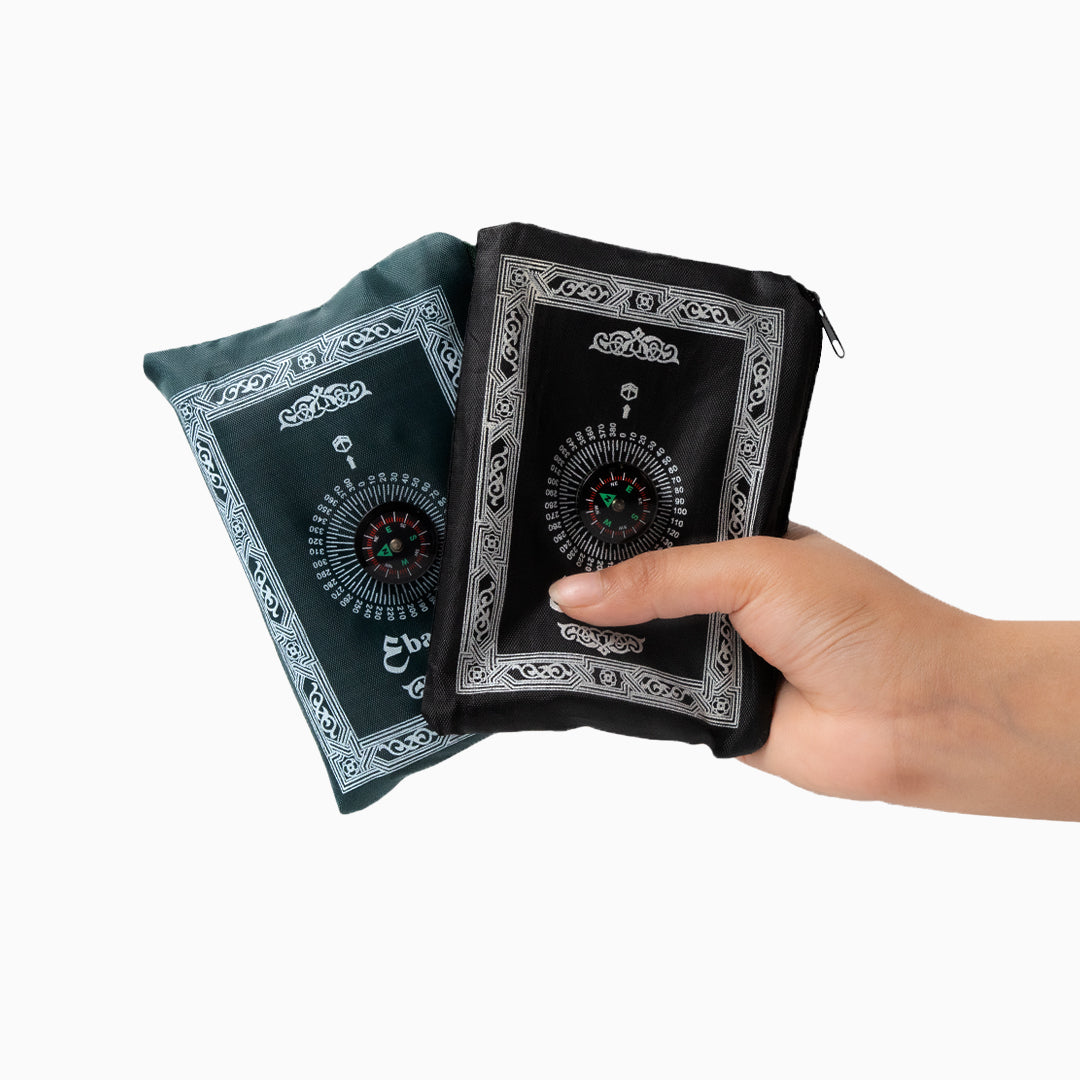 A Hand holding a black and green portable prayer rug