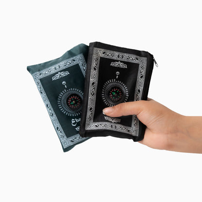 A Hand holding a black and green portable prayer rug